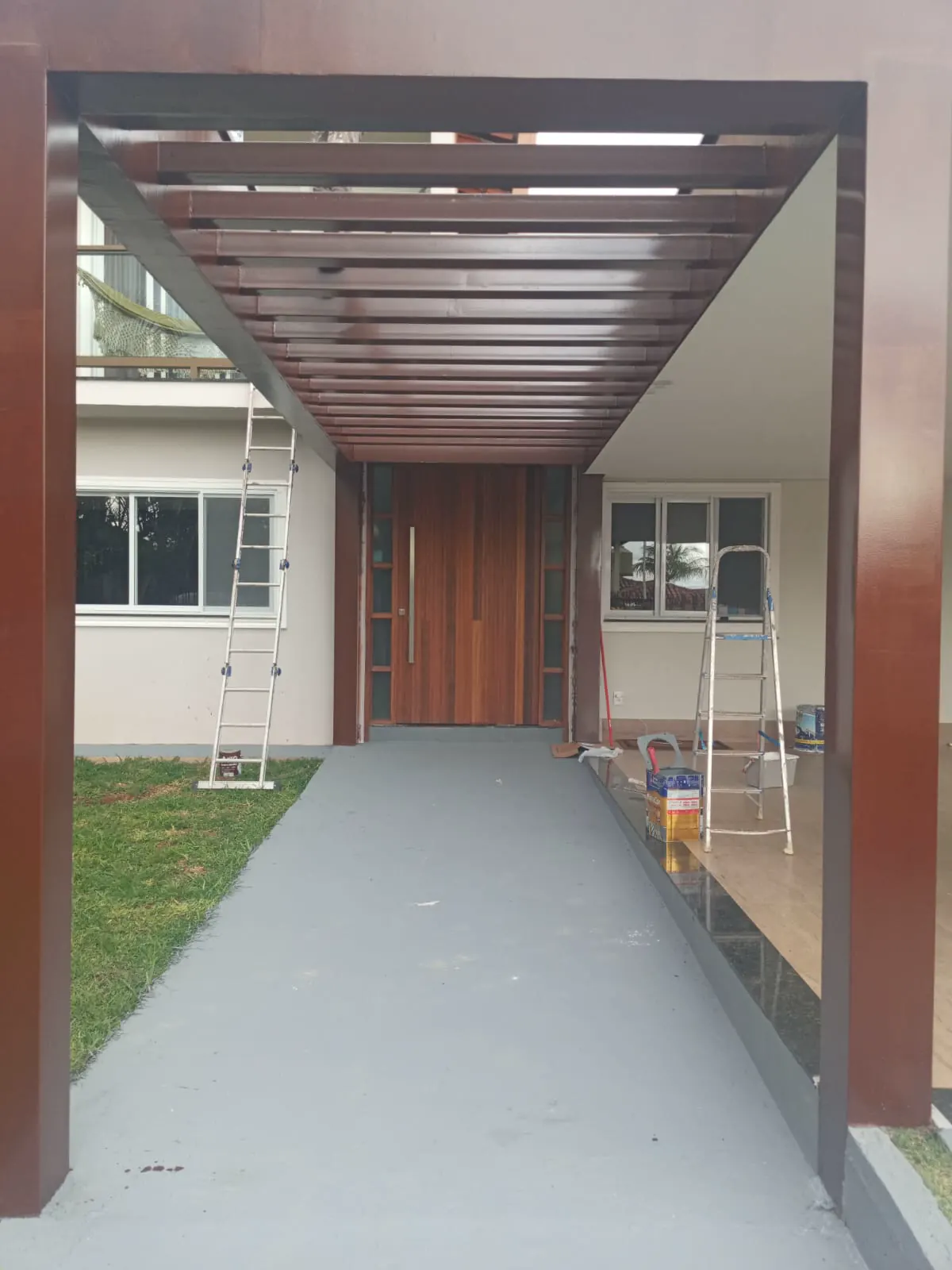 Entrada de casa com pergolado de madeira e pilares pintados, durante a execução