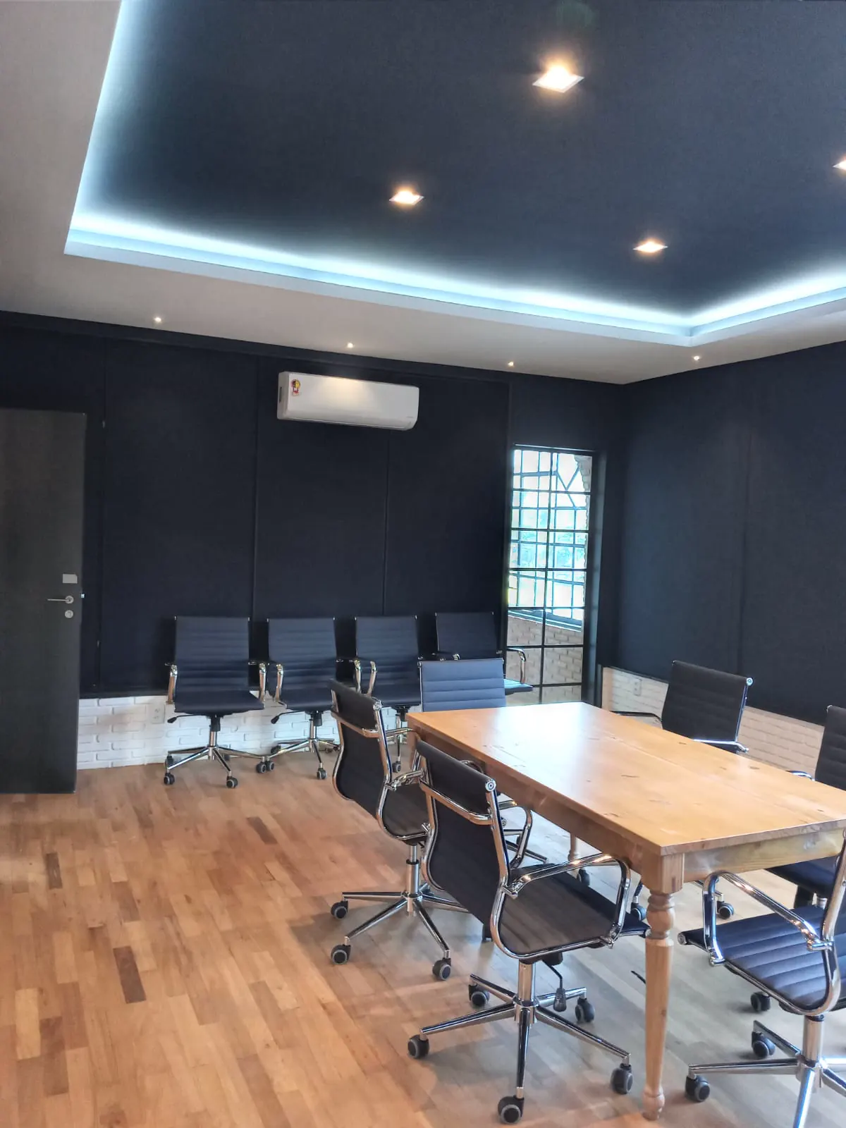 Sala de reunião com paredes e forro pintados em azul escuro, sanca iluminada e piso de madeira