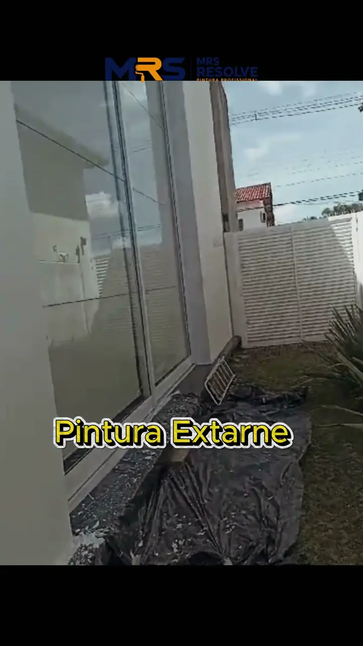 Parede externa de casa recém-pintada, com o piso protegido por lona durante o serviço
